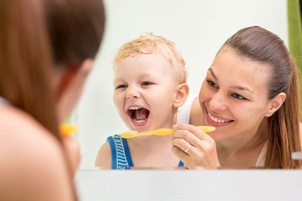 Mother teaching child how to brush their teeth in mirror