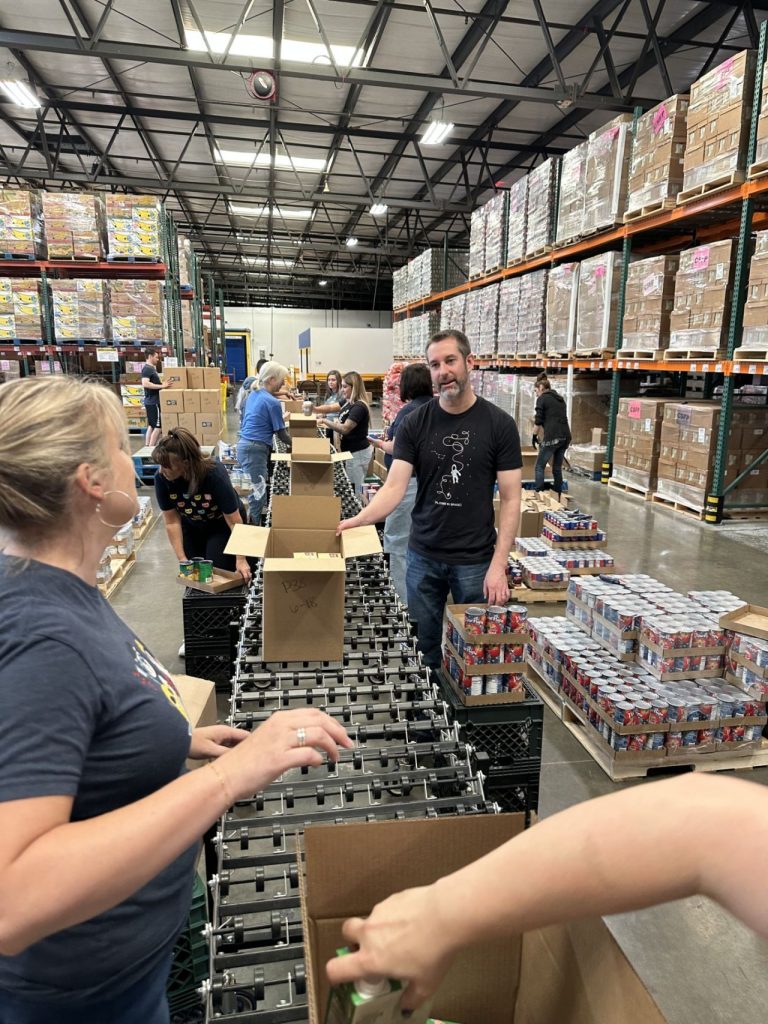 sacramento-food-bank-v3 A team member at Kids Care Dental & Orthodontics standing in front of donated food at the Sacramento Food Bank