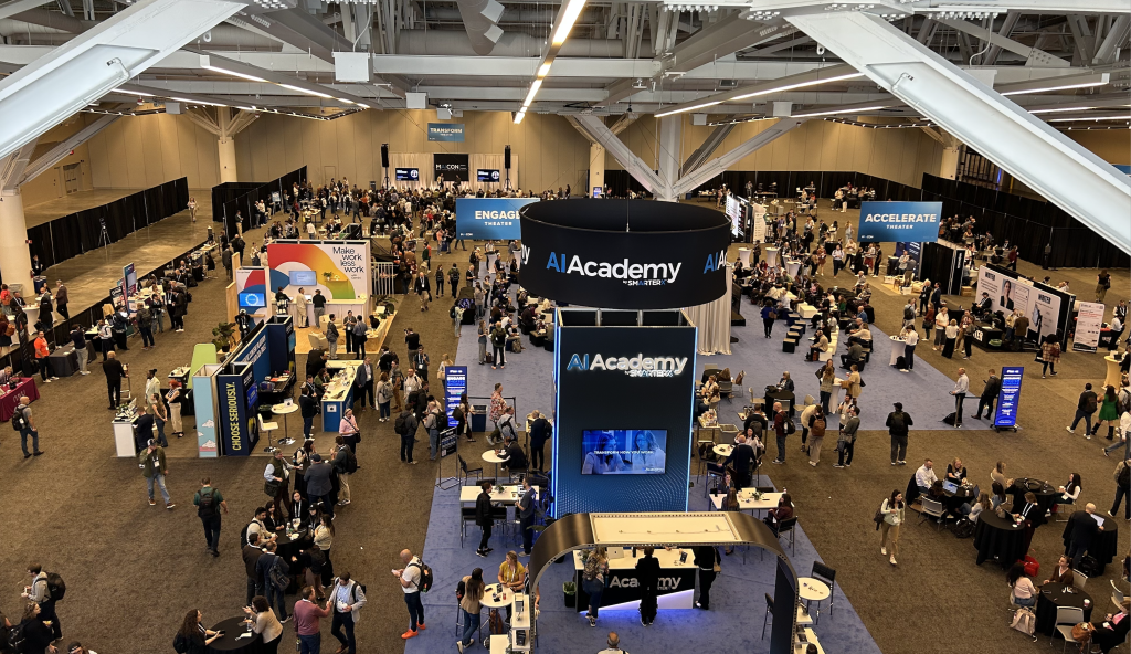 Overhead view of the MAICON 2026 exhibit floor in Cleveland, with attendees around the SmarterX AI Academy booth and vendor stands