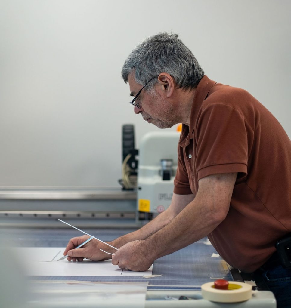 Yan, Head of Design at Pak-Pro, trimming a structural packaging prototype on a sample-cutting table.